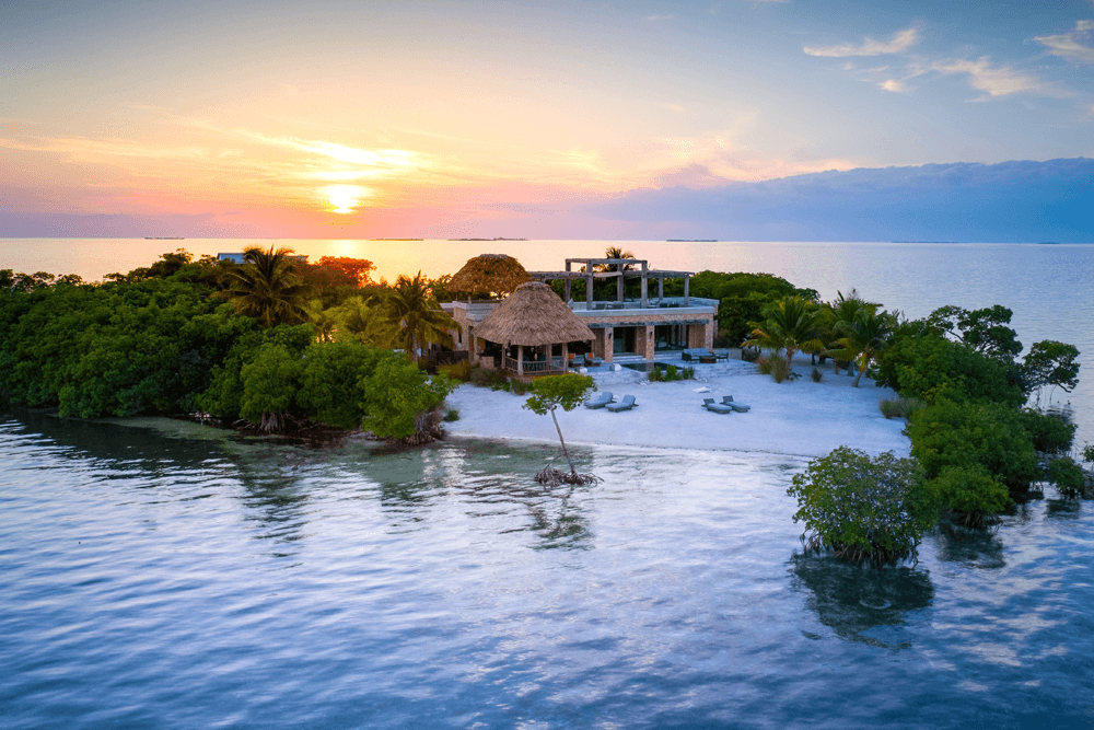 A serene private island with lush greenery and a beachside villa at sunset.
