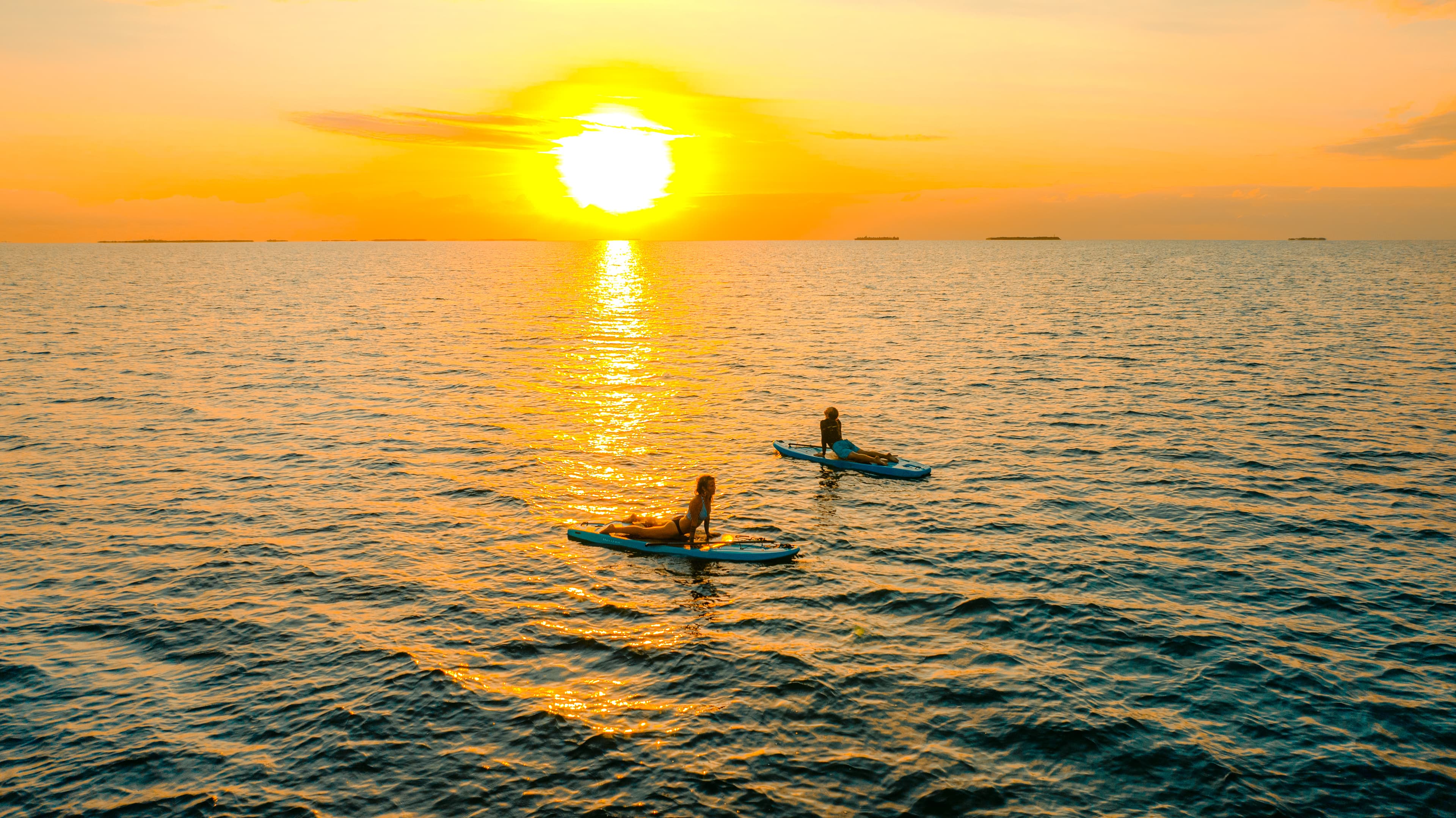 Two people paddleboarding on a tranquil sea at sunset.
