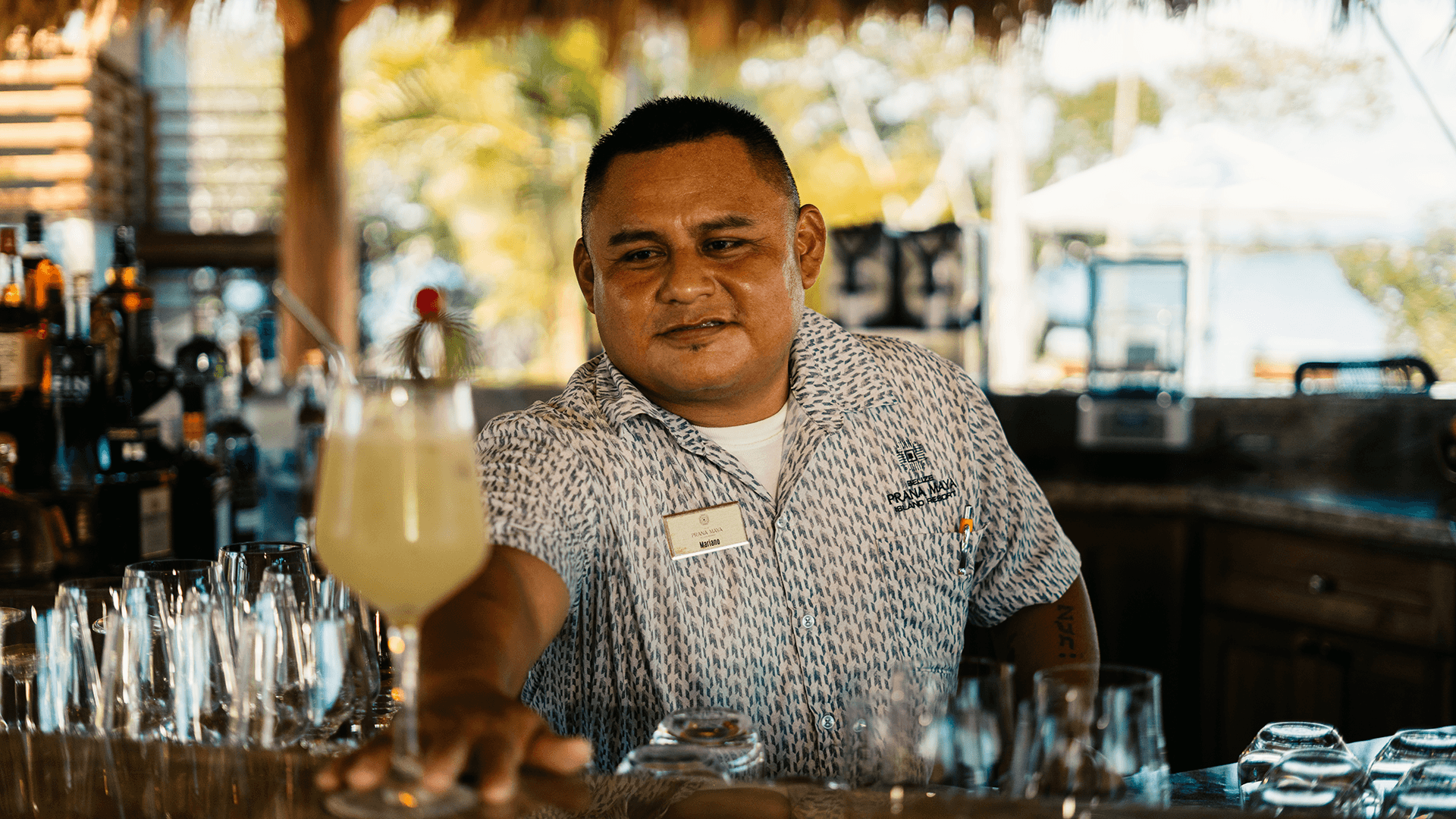 A bartender is serving a drink at a tropical bar.