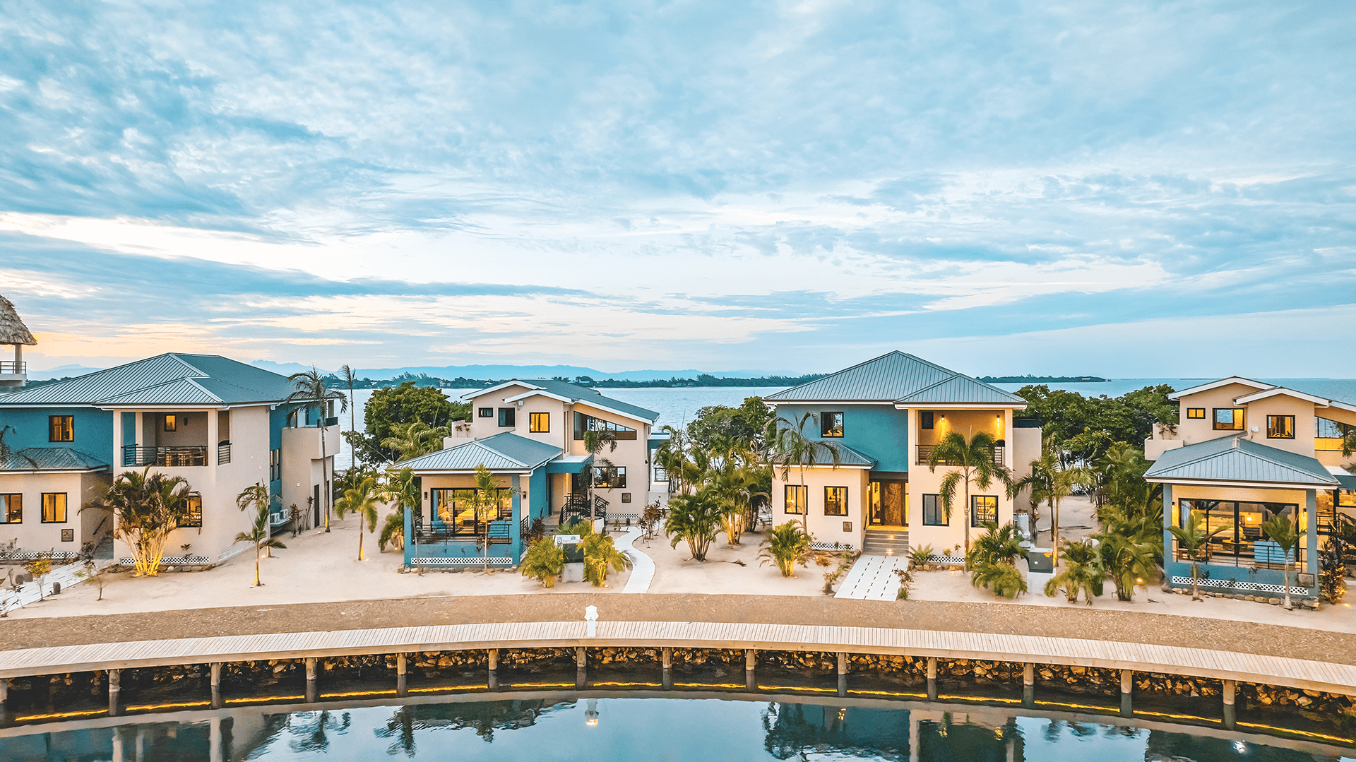 Aerial view of modern waterfront houses surrounded by palm trees and tranquil water.